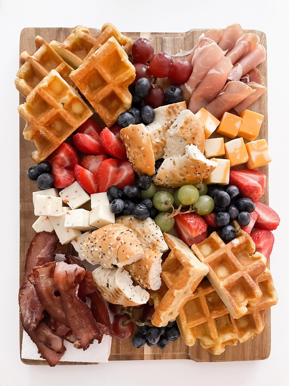 Easy breakfast idea - brunch board with waffles, strawberries, bagels, bacon, proscuitto, cheeses and more! 